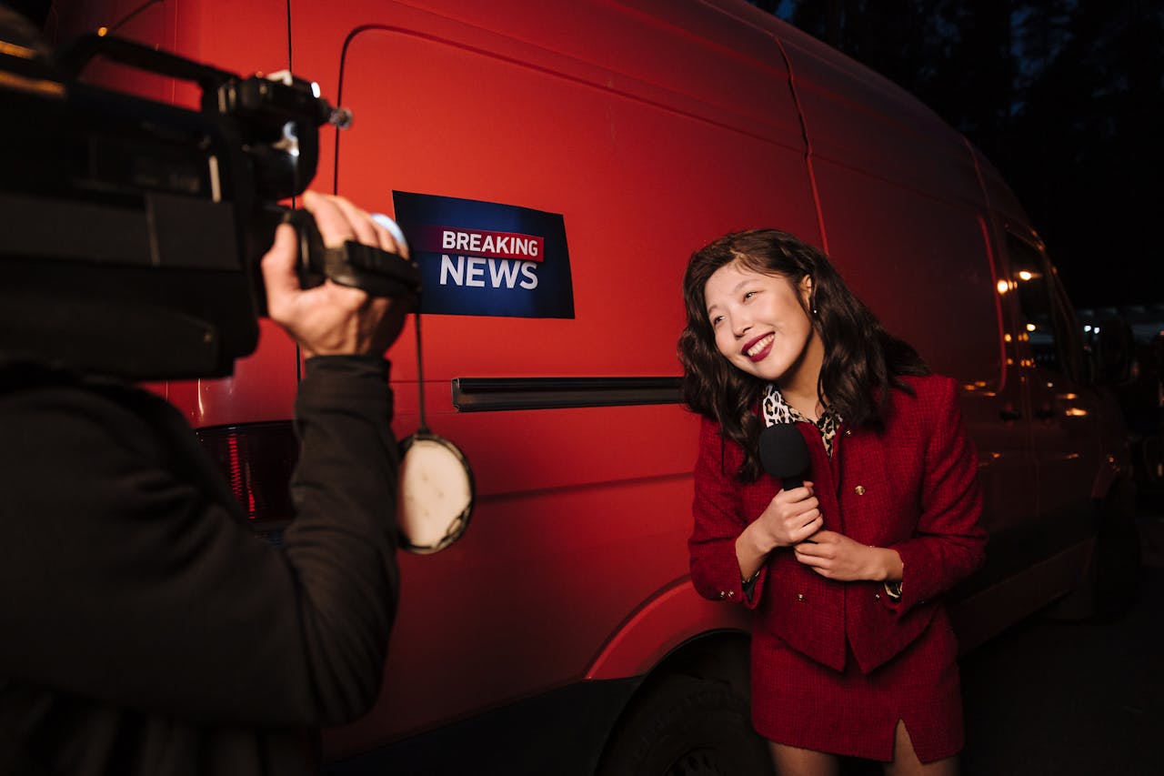 Asian female reporter in a red blazer reporting live on the news outdoors in the evening.