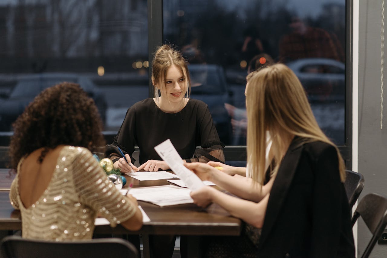 Three women engaging in a business meeting at an office table during nighttime.