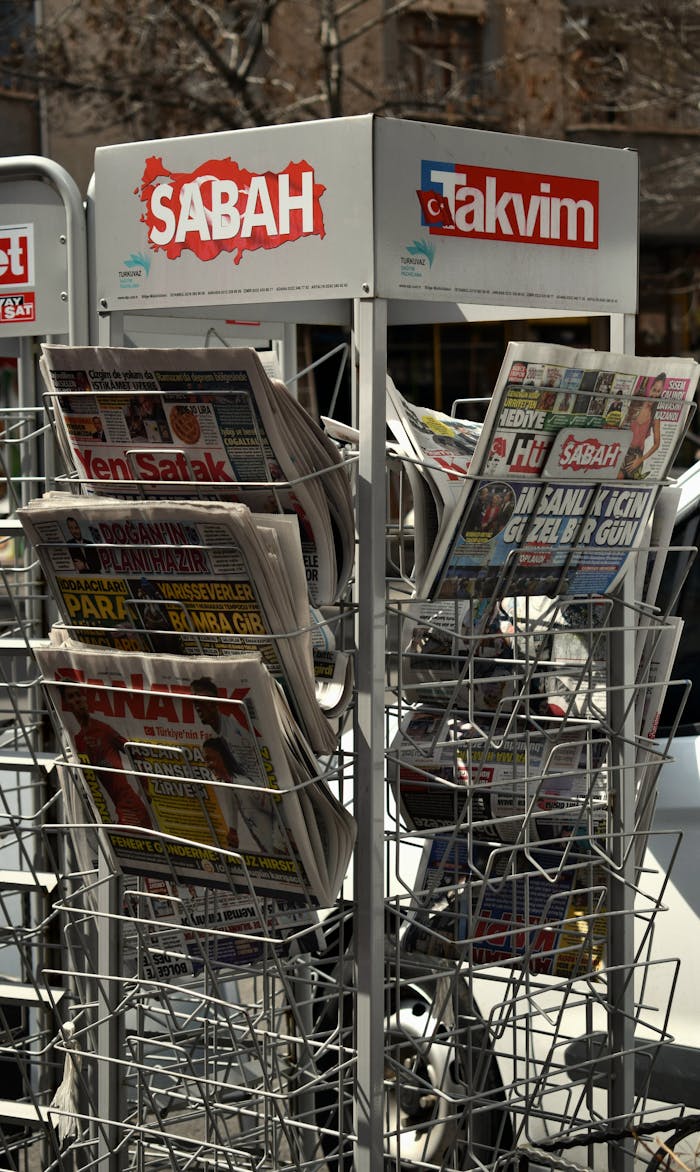 Outdoor newspaper rack holding various Turkish publications including Sabah and Takvim.