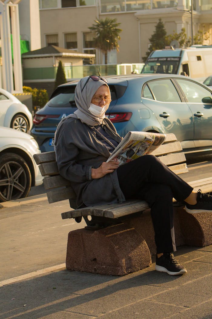 Elderly woman in health mask reading a newspaper on a sunny day.